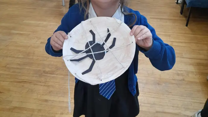 Child holding a piece of art featuring a spider and web.