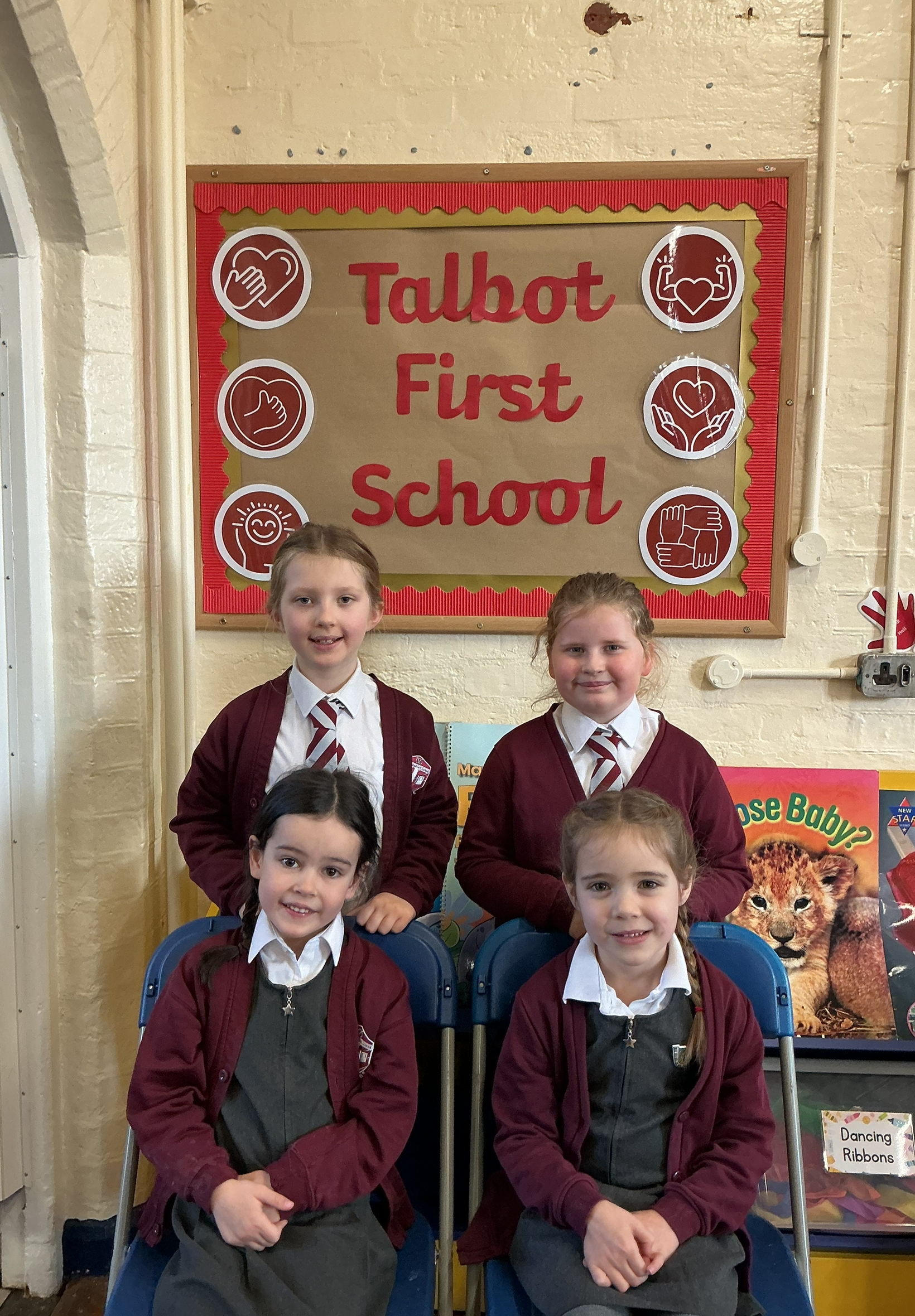 Four children smiling in front of a school poster.
