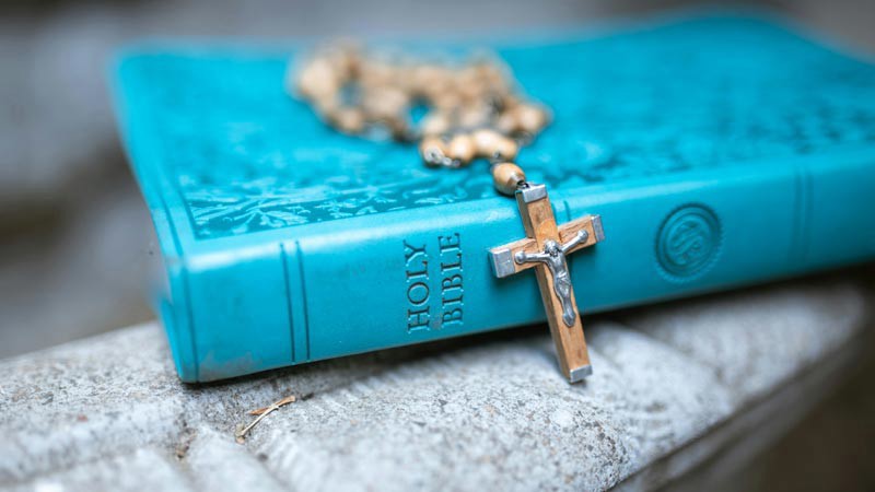 A copy of the Holy Bible with a rosary placed on top.