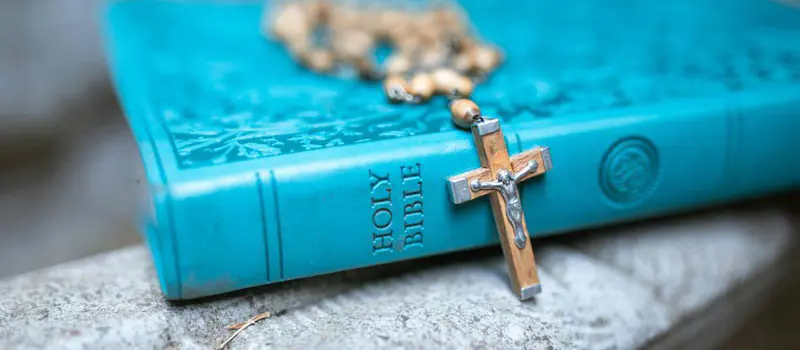 A copy of the Holy Bible with a rosary placed on top.