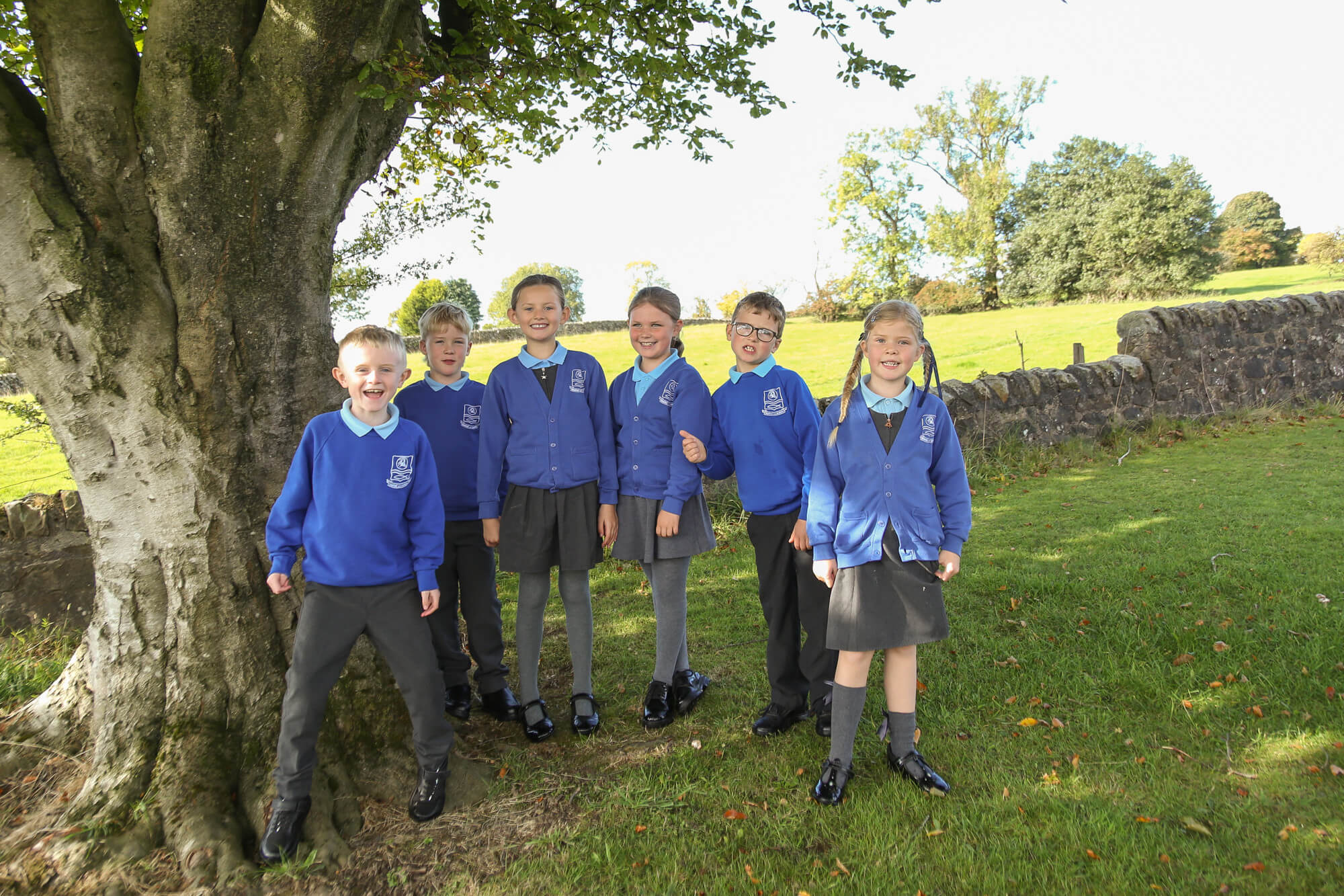 Children standing by a tree, smiling.