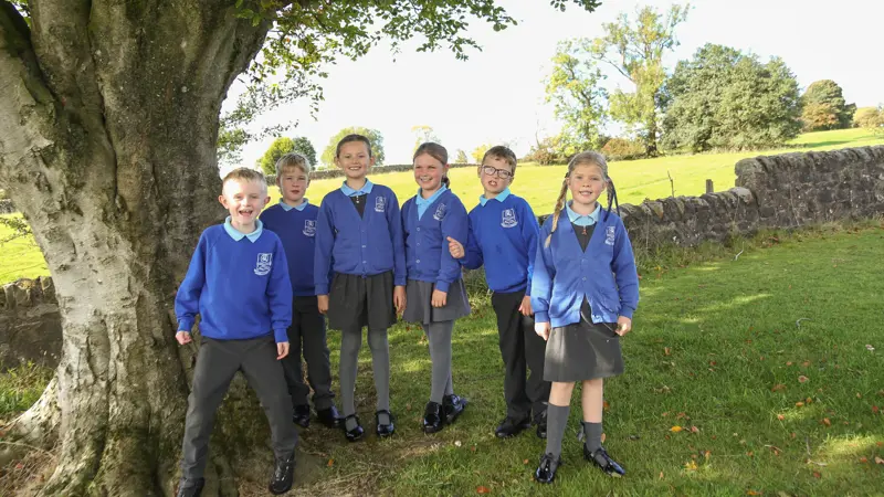 Children standing by a tree, smiling.
