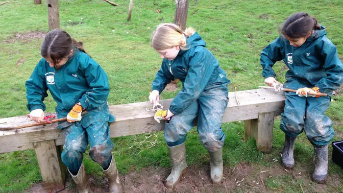 Three children shaping wood during a Forest School session.