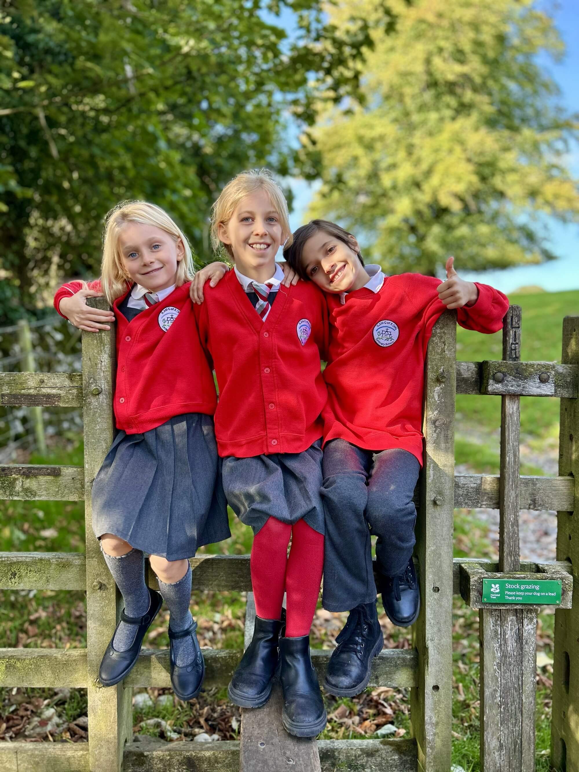 Three children smiling by a fence.