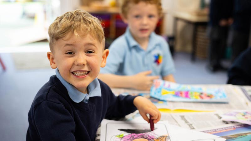 Child smiling to camera whilst colouring a picture.