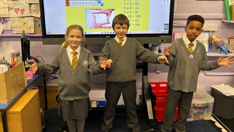 Three children standing together in a Maths lesson.