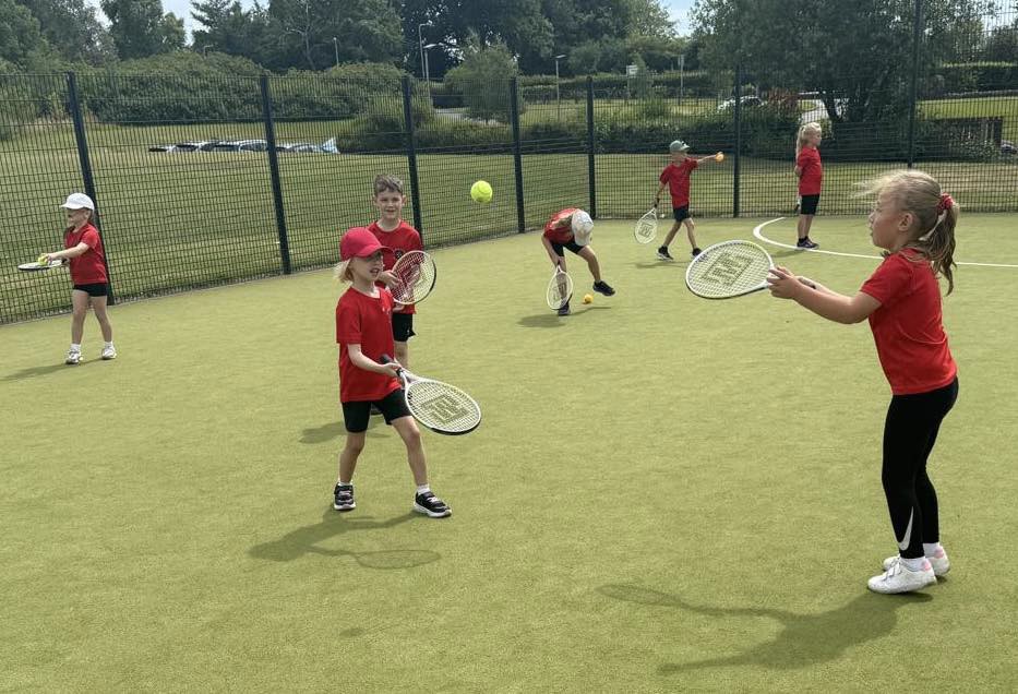 Children learning to play tennis in a PE lesson.