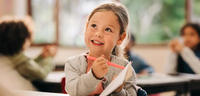 Smiling child pointing to her work with a pencil.