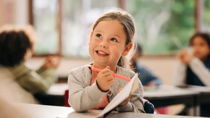 Smiling child pointing to her work with a pencil.