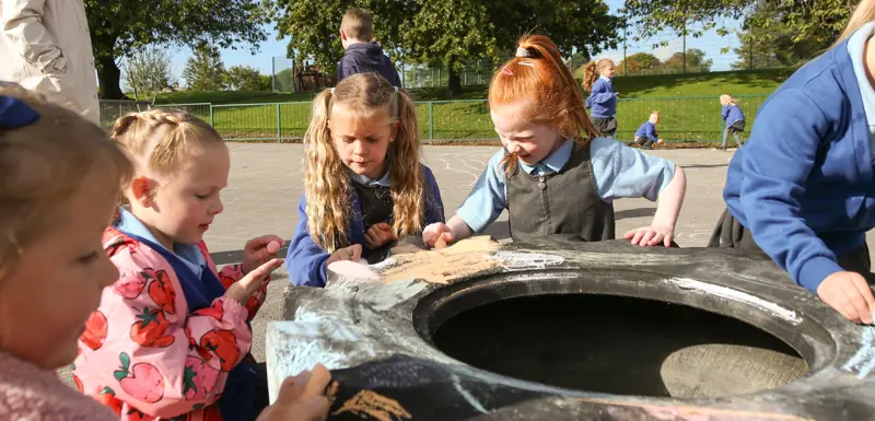 Children colouring and drawing on a play tyre.